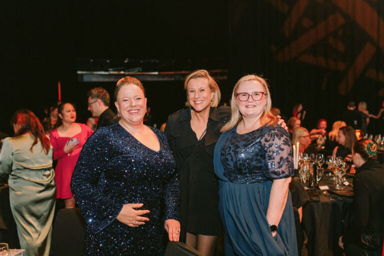 3 women at a black tie event smiling