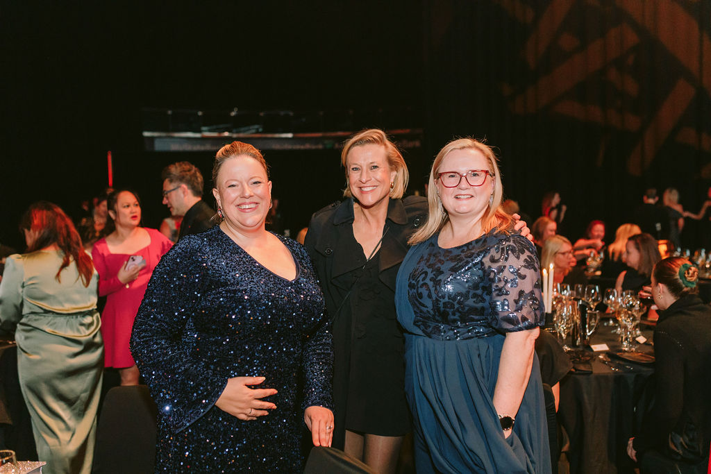 3 women at a black tie event smiling