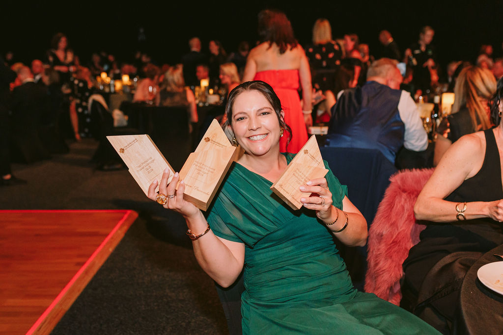 woman holds up 3 awards, conferece